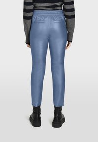 Blauwe neplederen broek met een slim fit, met een elastische tailleband en achterzakken, gedragen met zwarte plateauboots.