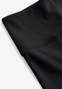 Black athletic fabric with a smooth texture, folded with a flat edge and reinforced stitching, highlighting its stretchable properties.