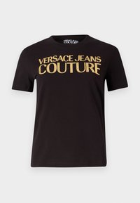 Juodas medvilnės marškinėliai su dideliu auksiniu tekstu "VERSACE JEANS COUTURE". Klasikinis apvalios iškirptės dizainas su trumpomis rankovėmis ir tiesiu apačia.