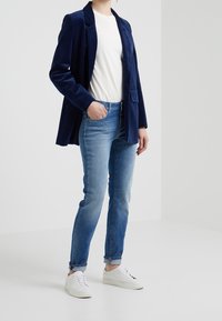 Námořnický kordový blejzr přes bílé tričko, spárovaný se světle modrými džíny a bílými teniskami. Blejzr má klopu a přední kapsu.