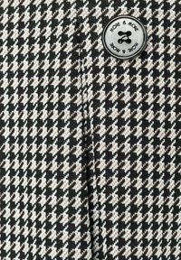 Zwart, wit en bruin houndstooth-patroon stof met een soepele textuur; bevat een ronde zwarte knop met het label "MEER & MEER."