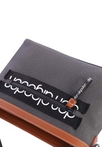 Bolsa textil gris con fondo de cuero marrón, con cremallera negra y marca blanca en el frente. Textura suave, forma rectangular.