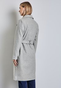 Jasnoszary płaszcz z wełny z kołnierzem, długimi rękawami i związanym paskiem w talii. Posiada proste linie i długość do połowy uda.