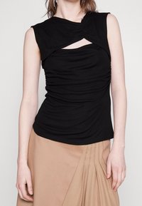 Top aderente nero con un design arricciato sul seno, scollo torcigliato e maniche corte. Tessuto morbido e elastico con una texture liscia.