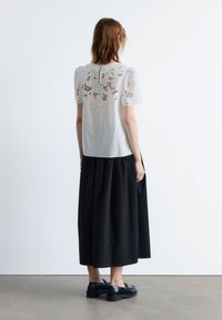 White blouse with lace yoke and short puff sleeves, paired with a black maxi skirt and black platform shoes. Smooth fabric, layered design.