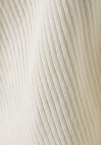 Ribbat tyg i off-white, med fina vertikala ränder och en mjuk textur, lämplig för kläder eller polstring.