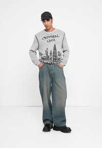 Grijze sweater met een stadsgezicht grafiek en de tekst "CENTRAL LDN." Gecombineerd met losse, vervaagde blauwe jeans en zwarte chunky schoenen.