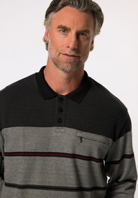 Camisa polo a rayas a cuadros con cuello negro y tres botones, que presenta tonos grises y negros con líneas de acento rojas.