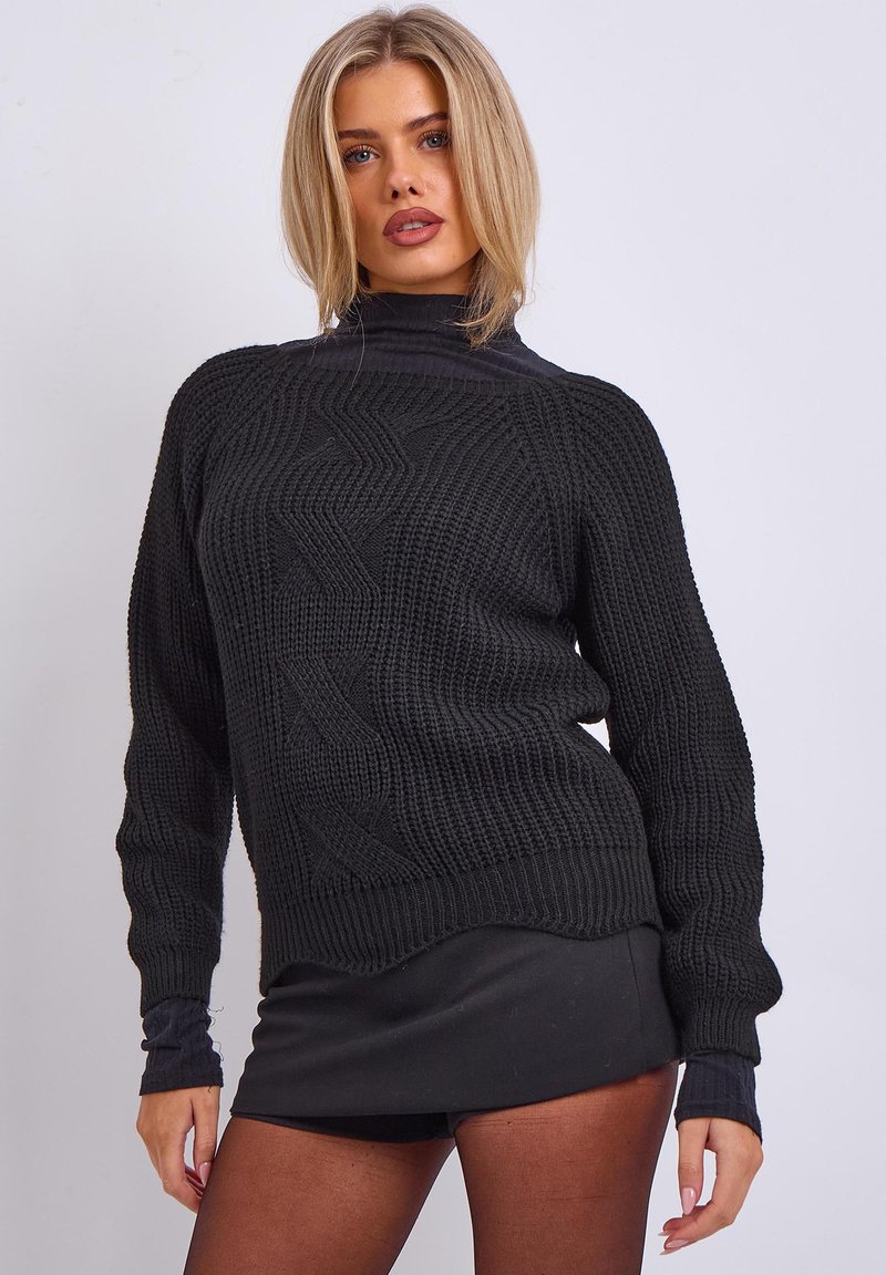 Schwarzer Strickpullover mit hohem Kragen, strukturiertem Muster und gerippten Bündchen. Über einem schwarzen Rock getragen, der einen abgerundeten Saum hat.