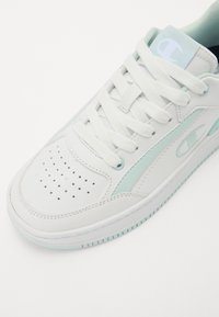 Fehér sneaker világoskék kiegészítőkkel, sima bőrből készült, perforált orral és vastag fehér fűzőkkel. Diszkrét logó található az oldalán.