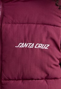 Maroon puffer vest featuring quilted texture, a full zipper, and embroidered "SANTA CRUZ" logo on the left chest area. Soft material.