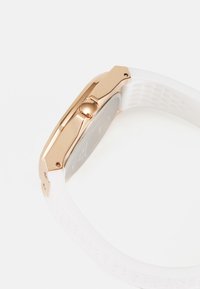 Zegarek kwarcowy z białym silikonowym paskiem i różowozłotą stalową kopertą. Posiada teksturowaną koronkę oraz elegancki, prostokątny design.