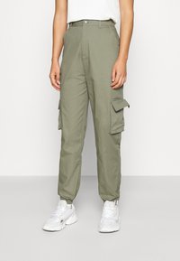 Olivgröna cargo-byxor med hög midja, med sidofickor, rak bendesign och elastiska muddar. Bärs med vita sneakers.