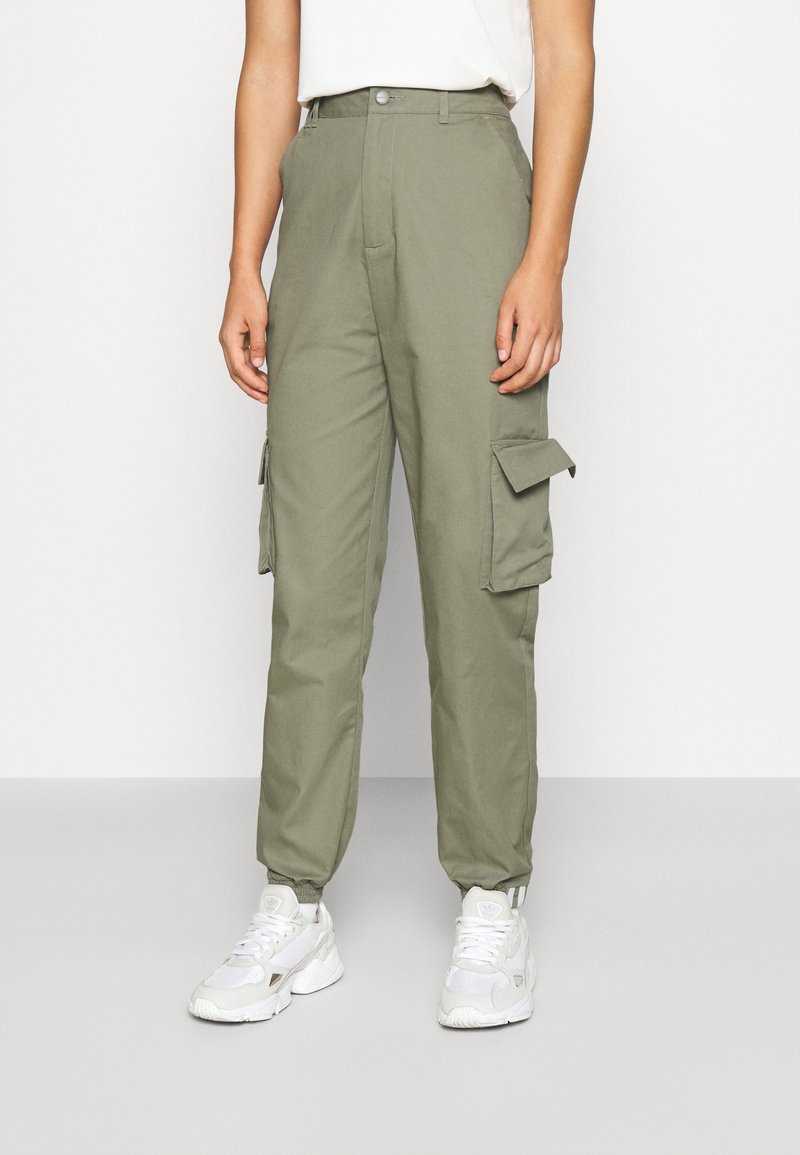 Olivgröna cargo-byxor med hög midja, med sidofickor, rak bendesign och elastiska muddar. Bärs med vita sneakers.
