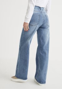 Helle blaue, hochtaillierte weite Jeans aus Denim, mit zwei Gesäßtaschen und lockerer Passform, kombiniert mit weißen Schuhen.