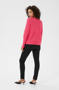 Pull en tricot fuchsia à manches longues, avec des bords côtes au niveau des poignets et de l'ourlet. Associé avec un jean noir ajusté et des escarpins noirs à bout pointu.