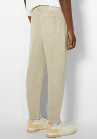 Pantaloni beige a sigaretta realizzati in morbido cotone, dotati di due tasche posteriori e di un'etichetta in vita. Abbinati a scarpe da ginnastica di colore chiaro.