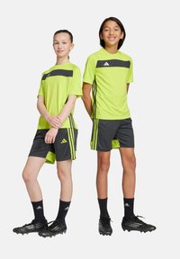 Ropa deportiva juvenil que incluye camisetas de un brillante verde neón con detalles en negro, pantalones cortos negros con ribetes verdes y botas de fútbol negras.