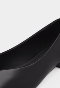 Chaussure pour femme noire à talon bas avec un bout arrondi et une finition en cuir lisse, inclinée pour montrer le côté et une partie de l'intérieur.