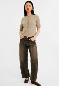 Beige gekruiste gebreide cardigan met korte mouwen en een ronde halslijn, voorzien van vijf knopen, gecombineerd met een paar bruine denim jeans met wijde pijpen en donkerbruine flats.