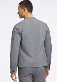 Grå långärmad jacka i texturerat tyg, med rak skärning, knäppta ärmslut och en ren, minimalistisk design.