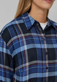 Blau-schwarz kariertes Flanellhemd mit Knopfverschluss, das kontrastierende weiße und rote Linien aufweist, einen strukturierten Kragen hat und eine weiche Textur bietet.