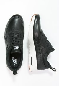 Svarta lädersneakers med en jämn textur, med en vit mellansula, svarta snören och en perforerad sektion. Nike-logotypen på tungan.