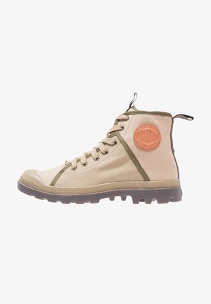 Beżowy sneaker za kostkę z płótna z brązową gumową podeszwą, zielonym wykończeniem, sznurowadłami, pętelkami i okrągłą skórzaną naszywką z logo na kostce.