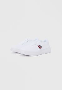 Beli športni copati z zgornjim delom iz teksturirane tkanine, okrogel nos, gumijast podplat z rdeče-črto črtastim poudarkom na strani.