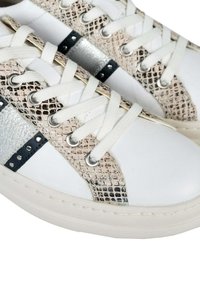 Zapatillas blancas con un patrón de piel de serpiente texturizado en beige y acentos metálicos en plata, con cordones blancos y ojales redondos en plata.