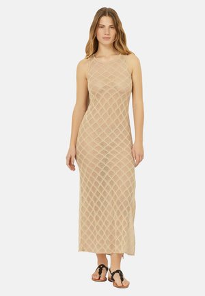 Knee-length, beige knit dress with a diamond pattern, sleeveless design, and a crew neckline. Paired with black sandals.