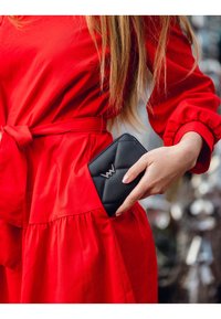 Black quilted wallet with a silver logo, partially visible in a red dress pocket. The fabric is smooth with a structured design.