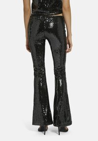 Zwarte pailletten flared broek met een glanzende textuur, voorzien van een aansluitende taille en wijde pijpen. Draagt een bijpassende crop top.