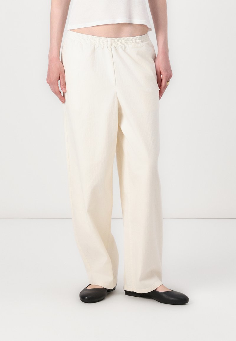 Witte, ruime broek met een elastische tailleband, gemaakt van lichte stof. Gecombineerd met zwarte platte schoenen. Eenvoudig en veelzijdig ontwerp.