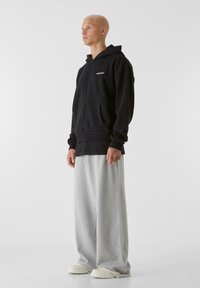Svart zip-up hoodie med kängurufickor, tillsammans med vida grå sweatpants. Har en logga på bröstet och ett mjukt, strukturerat tyg.