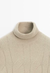 Beiger, gerippter Rollkragenpullover aus weichem Strickmaterial mit engem Kragen und dezenten, durchgehenden Strukturmustern.