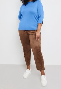 Pull en tricot bleu à manches trois-quarts, associé à un pantalon court en suède marron et des baskets blanches. Tenue simple et décontractée.