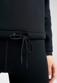 Zwarte sportkleding met een gladde textuur, afgeronde zoom en een koordsluiting met zwarte aglets voor een verstelbare pasvorm.