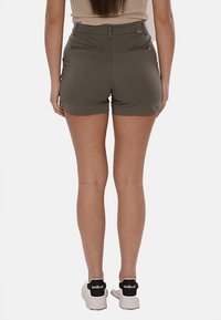 Pantaloni corti verde oliva con un design aderente, dotati di tasche posteriori, una superficie liscia e orlo arrotolato, abbinati a sneakers bianche.