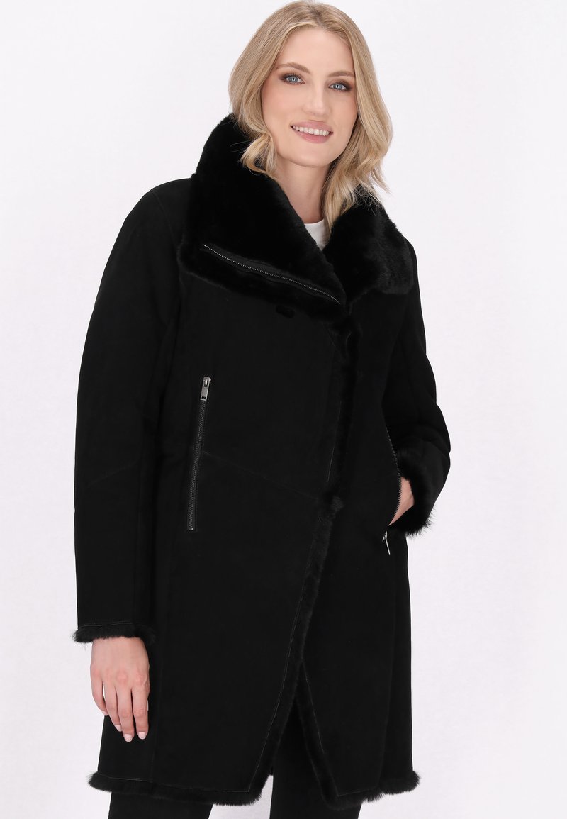 Cappotto in finta pelliccia nera foderato, con ampio colletto, tasche con zip, finitura testurizzata e lunghezza fino al ginocchio.