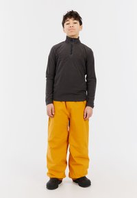 Fleece coltrui in donkergrijs met een rits, gecombineerd met losse oranje waterdichte broek. Zwarte schoenen maken de outfit compleet.