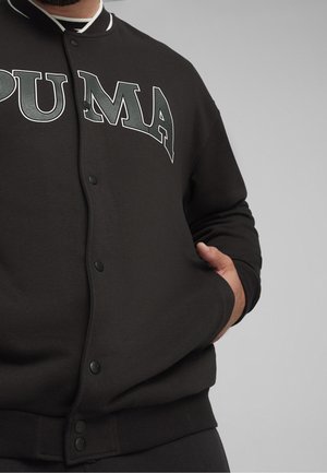 Sudadera negra con cierre de botones en el frente, cuello blanco y un gran logo "PUMA" en gris en el pecho. Cuenta con puños y cintura acanalados.