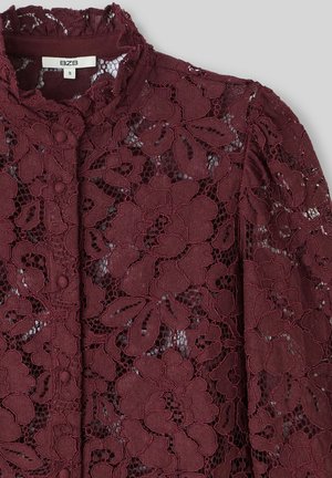 Blouse en dentelle bourgogne avec des motifs floraux, col montant et détails de boutons. Texture transparente avec une apparence tactile et superposée.