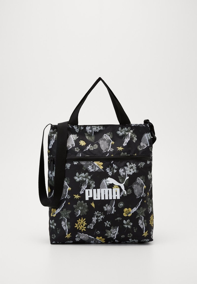 Black fabric bag with floral patterns in grey, yellow, and green. Features top handles and an adjustable strap. Large white logo on front.