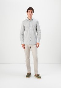 Button-up shirt in light gray with a subtle pattern, paired with light beige trousers and green shoes, featuring a textured sole.