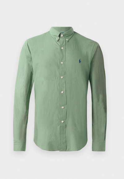 Zelena srajca z gumbi iz lahkega materiala; ima ovratnik s konico, dolge rokave in majhen moder logotip na levem prsnem delu.