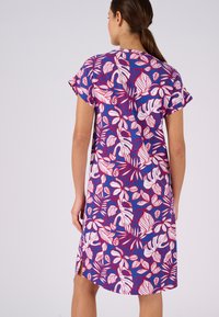 Abito a maniche corte in tessuto blu con un vivace motivo di foglie tropicali rosa e bianche, dotato di spacchi laterali per facilitare il movimento.