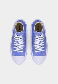 Ζευγάρι μωβ Converse χαμηλά παπούτσια με λευκά κορδόνια και λαστιχένιες άκρες στα δάχτυλα, φωτογραφημένα από πάνω σε λευκό φόντο.