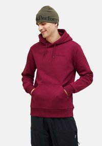 Felpa bordeaux con tasca frontale a canguro, cappuccio con cordino e polsini a coste. Abbinata a pantaloni neri con tasche con zip.