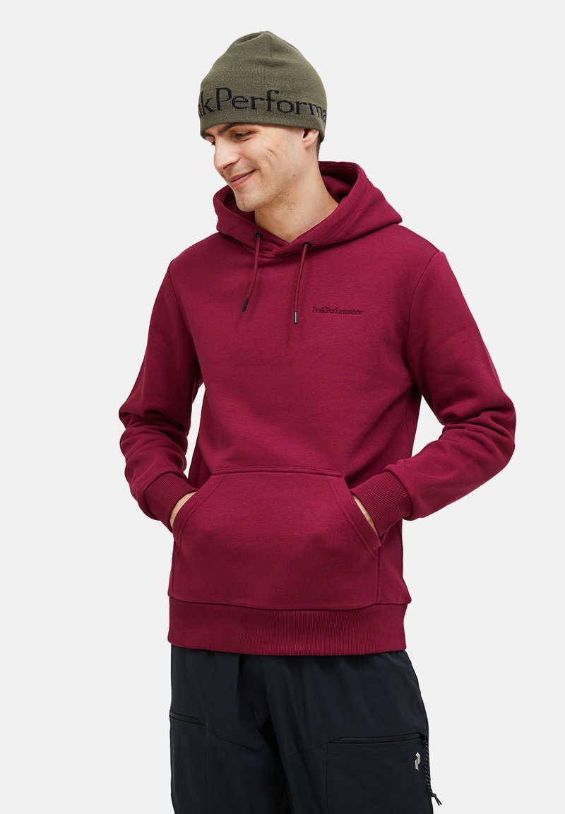 Felpa bordeaux con tasca frontale a canguro, cappuccio con cordino e polsini a coste. Abbinata a pantaloni neri con tasche con zip.